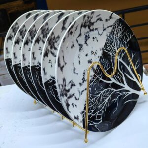 Elegant black and white ceramic dinner plates with a marble and tree branch design, neatly arranged in a gold metal rack – perfect for modern and luxury dining.
